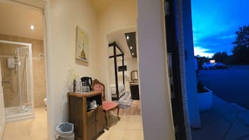 A hotel entrance with a glass door leading to a shower area, a small wooden cabinet, and a chair.