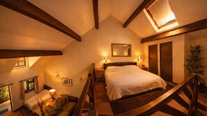 A bedroom with a sloped ceiling, a bed, a nightstand, a mirror, and a window with curtains. - Langford Apartments and Rooms (Bristol)