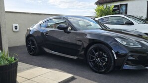 A black sports car parked in a driveway with a security camera and a potted plant nearby. - Langford Apartments and Rooms (Bristol)