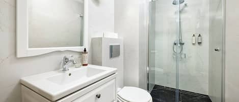 A modern bathroom with a white marble sink, a toilet, and a glass-enclosed shower area.
