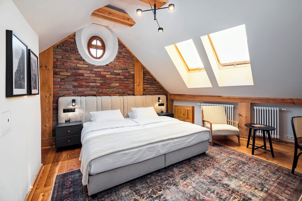 Une chambre avec un grand lit, un plafond en bois, un mur en briques et des fenêtres de toit.