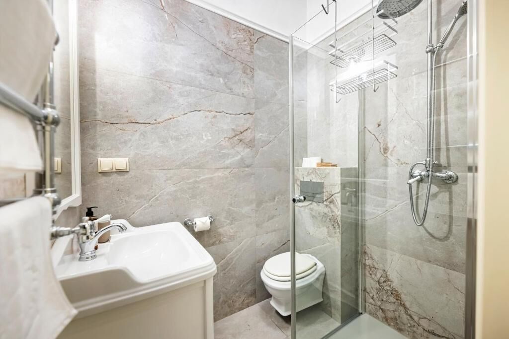 A modern bathroom with a glass-enclosed shower, a white sink, and a marble wall.