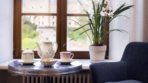 A table with a teapot, cups, and a bowl on a windowsill with a view of a castle. - Fontana Boutique (Lublin)