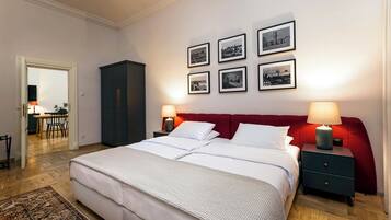 Un dormitorio ordenado con una cama grande, dos mesitas de noche con lámparas, un cabecero rojo y seis fotografías blanco y negro en la pared.