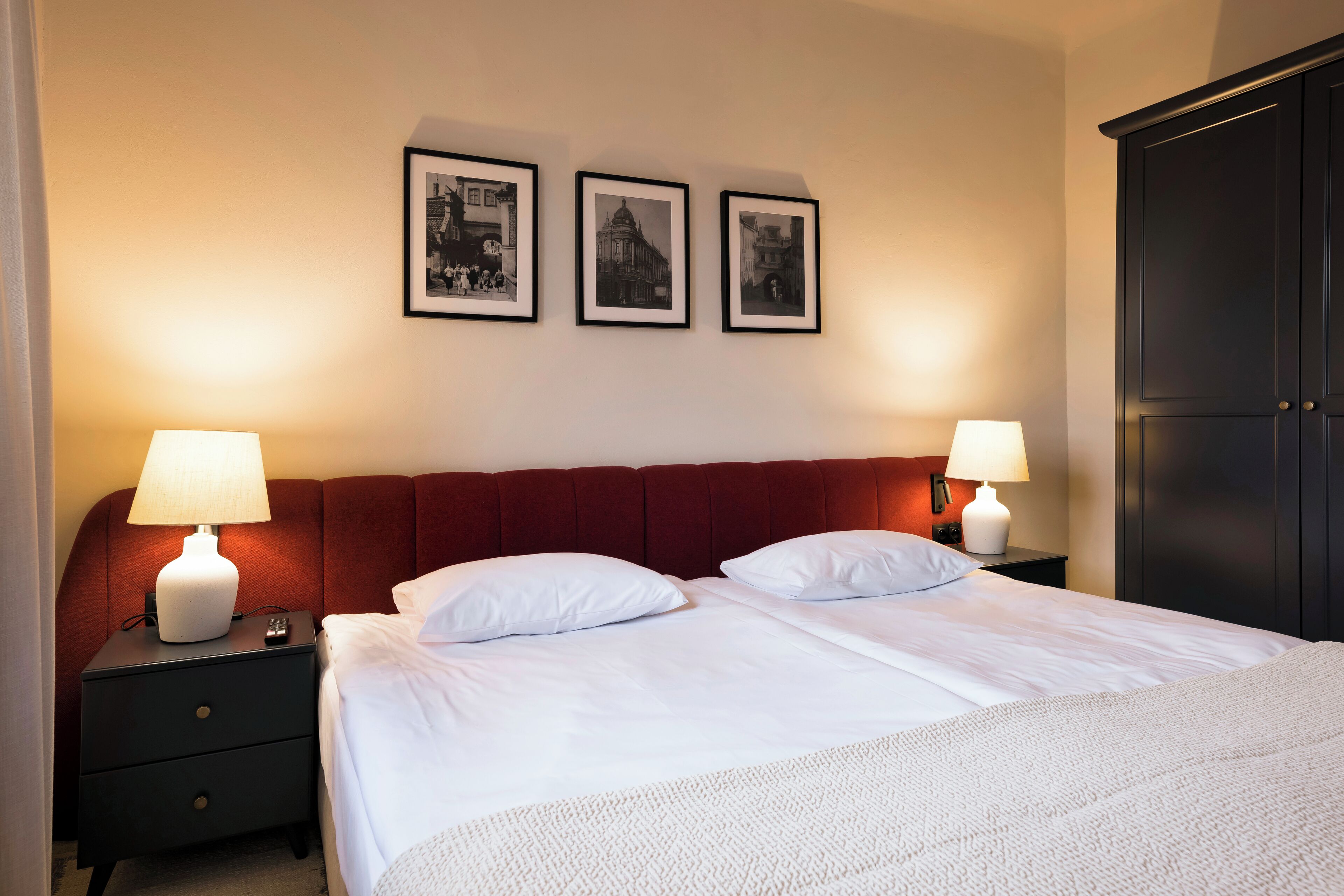 A hotel room with a large bed, two bedside tables with lamps, a wardrobe, and three framed pictures on the wall.