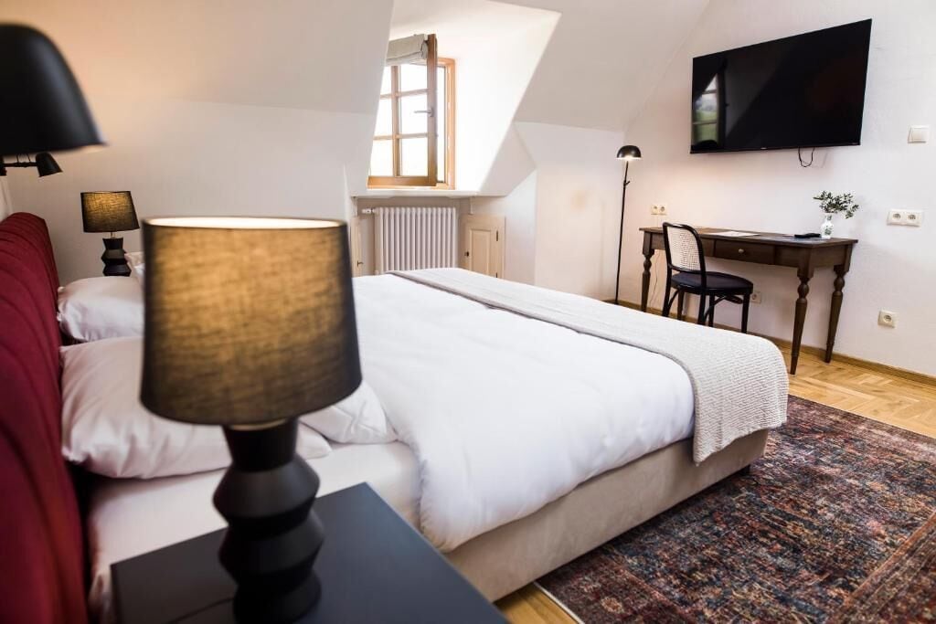A bedroom with a bed, a desk, a chair, a TV, and a lamp.