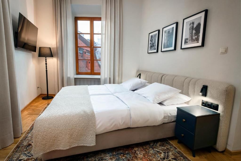Quarto bem arrumado com cama, mesa de cabeceira, abajur e quadros na parede.