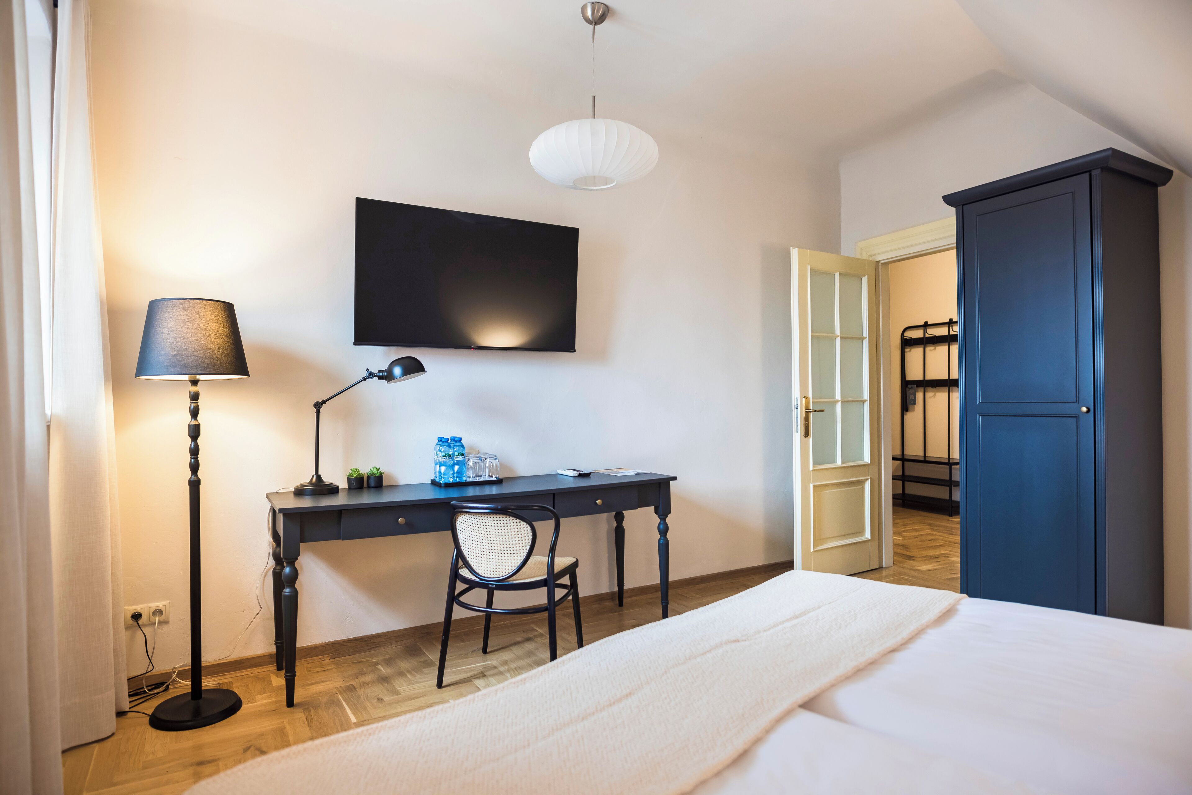 A bedroom with a bed, desk, chair, and a TV mounted on the wall.