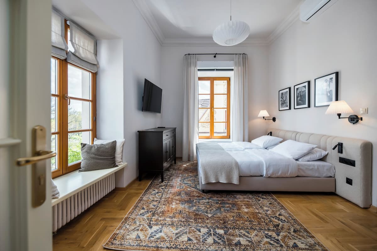 Une chambre à coucher comprenant un lit, un radiateur, une télévision, une fenêtre avec des rideaux et un tapis à motifs.