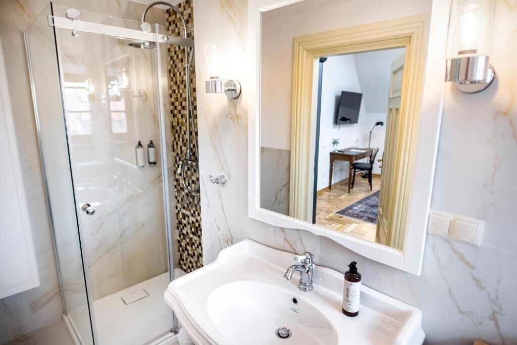 Un bagno con cabina doccia in vetro, un lavandino bianco e uno specchio che riflette una zona pranzo.