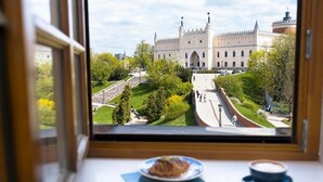 A view from a window of a building with a large, ornate structure in the background, a paved pathway, and a table with a plate and a cup. - Fontana Boutique (Lublin)
