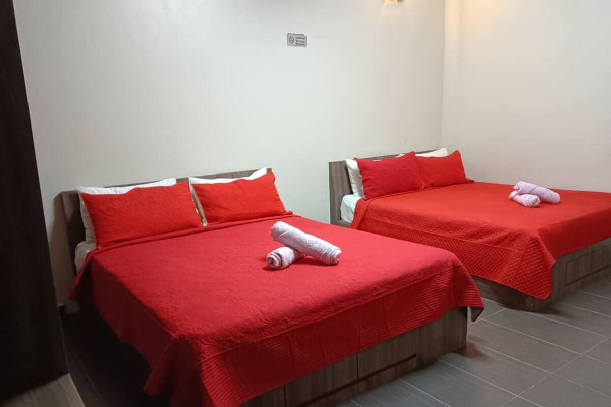 Two single beds with red bedding and white pillows, a small sign on the wall, and a tiled floor.