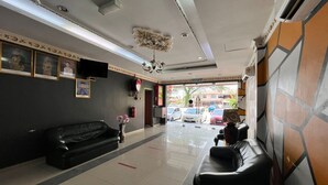 A lobby with a black leather sofa, a small table with a vase, framed pictures on the wall, and a chandelier. - Hotel O Ezi Inn (Kuala Kangsar)