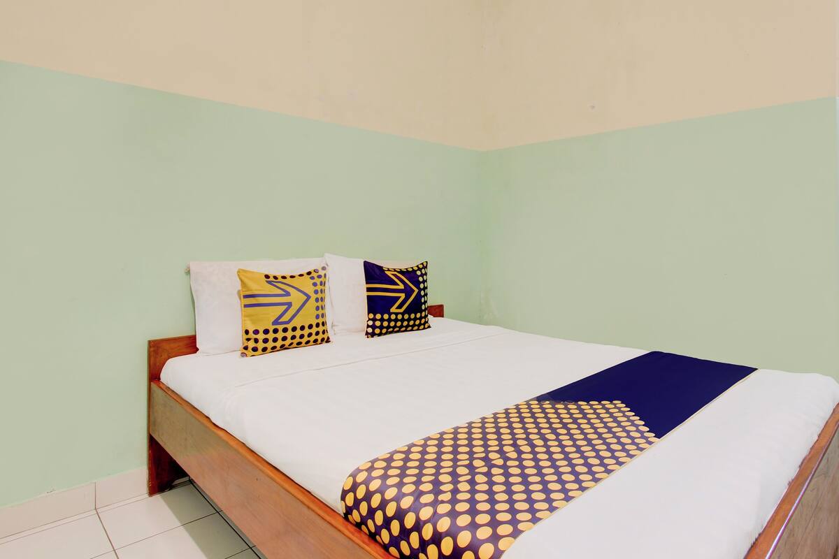 A bed with a white mattress, a blue and yellow patterned bedspread, and two pillows with geometric designs.