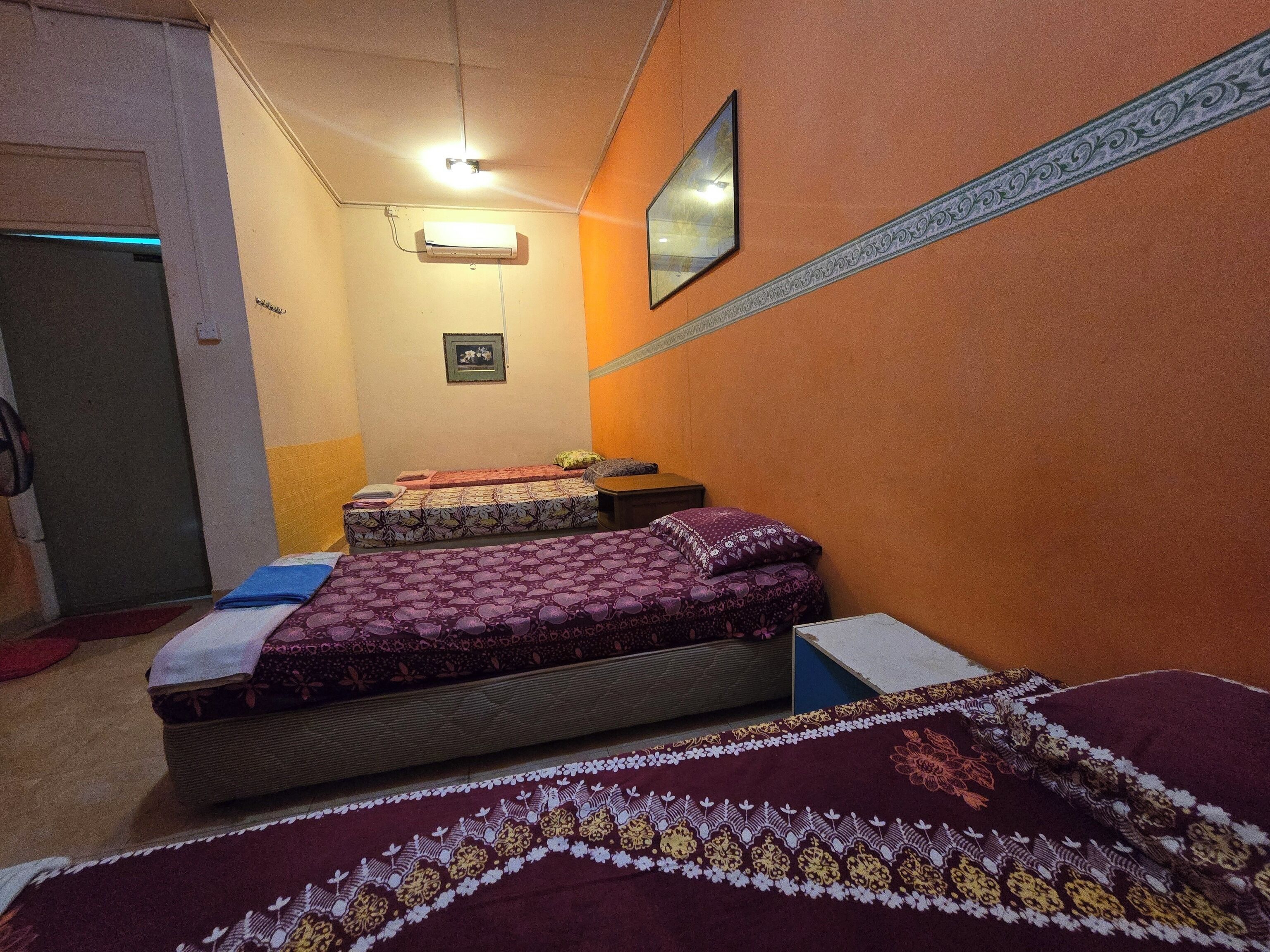 A room with two beds, a small table, a wall-mounted air conditioner, and a door.