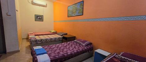 A room with two beds, a small table, and a wall-mounted air conditioner.