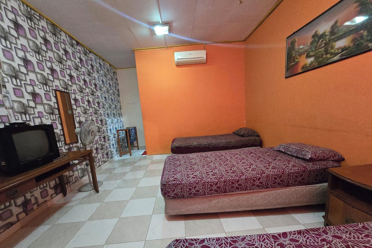 A room with two beds, a television on a wooden stand, and patterned wallpaper.