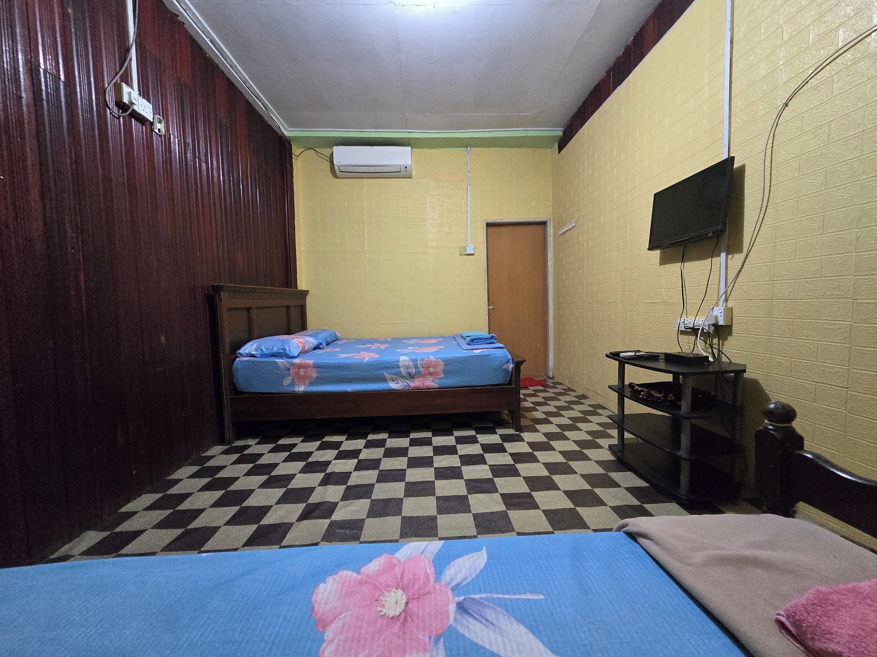 Una habitación con cama, una mesita, un televisor montado en la pared y una puerta.