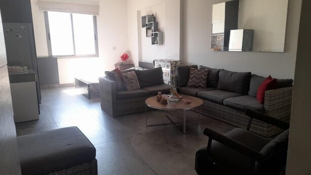 A modern living room with a sofa set, a coffee table, and a dining area with a refrigerator. - Loft in Dbayeh,including Generator, Prime Location (Dbayeh)