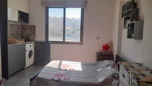 A compact bedroom with a bed, a small dresser, a washing machine, and a window with a city view. - Loft in Dbayeh,including Generator, Prime Location (Dbayeh)