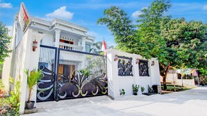 Un bâtiment blanc avec un portail noir, des plantes en pot et un drapeau.