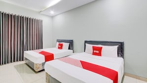 Une chambre d’hôtel avec deux lits, chacun agrémenté de draps blancs et de touches de couleur rouge, et un rideau sur le côté gauche.