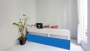 Un espace d’accueil avec un comptoir blanc, une plante en pot et des coussins colorés.
