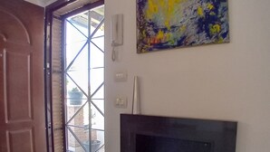 Een kamer met een houten deur, een glazen deur die naar buiten leidt, een open haard en een schilderij aan de muur.