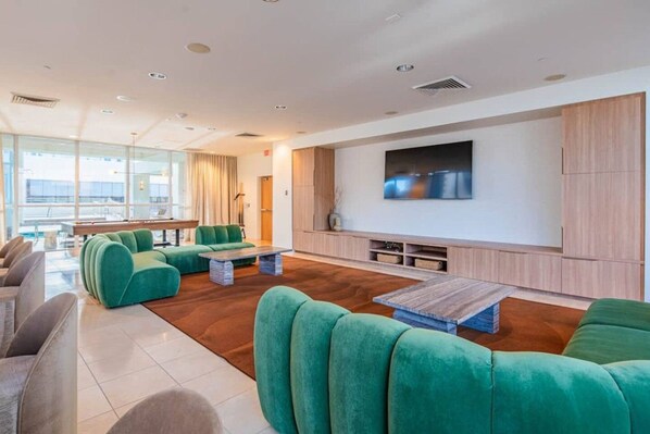 A modern living room with green sofas, a flat-screen TV, wooden cabinets, and a large window offering a view.