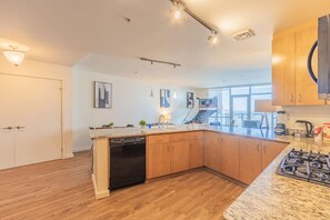 A modern kitchen with a dishwasher, granite countertops, wooden cabinets, and a gas stove.