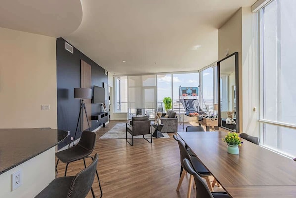 A modern living room with a dining area, large windows, and a view of the city.