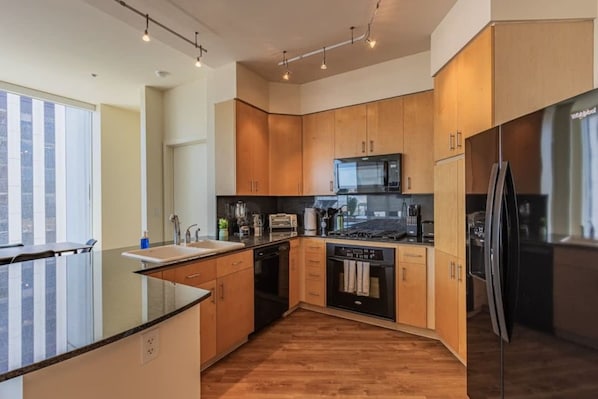 A modern kitchen with wooden cabinets, a black refrigerator, and a built-in microwave.