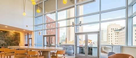A spacious indoor area with large windows, a central wooden table, and several chairs.