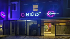 The Olive Hotel with a modern facade, large entrance gates, and prominent signage in multiple languages.