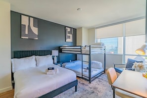 A hotel room with a bunk bed, a single bed, a desk with a chair, a lamp, and a large window. - Near ASU | Gym, Parking and Pool, Balcony & In-Uni (Phoenix)