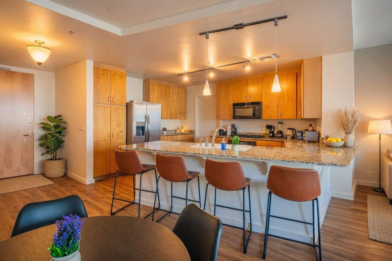 A modern kitchen with wooden cabinets, a central island with bar stools, stainless steel appliances, and pendant lighting.