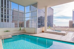 A rooftop pool with a city view, large windows, and a small hot tub.