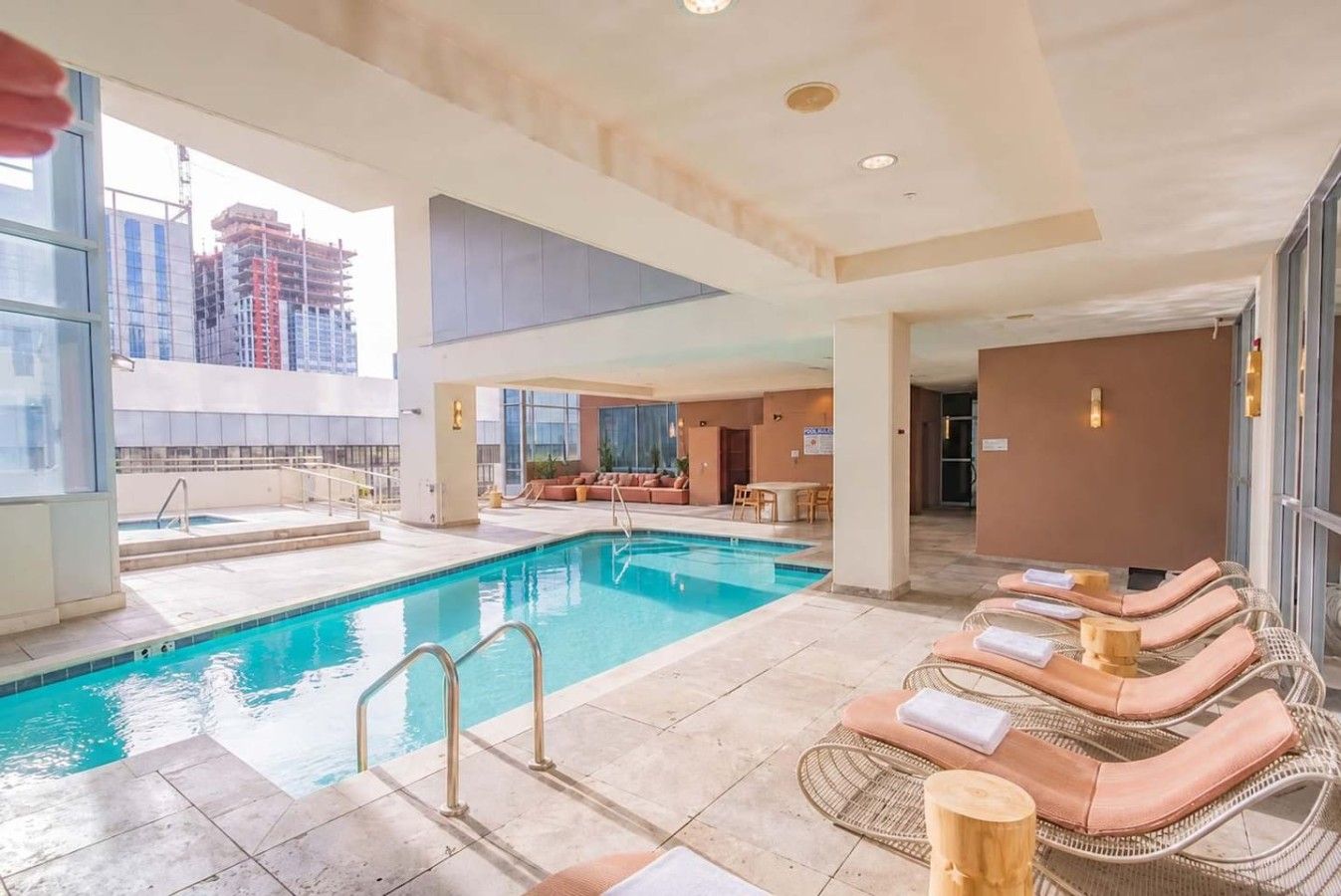 A hotel pool area with a clear view of the city skyline, a lounge area with sun loungers, and a separate section with a seating area and a table.
