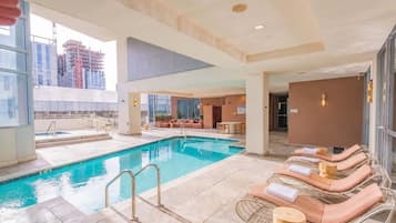 A hotel pool area with a clear view of the city skyline, a lounge area with sun loungers, and a separate section with a seating area and a table.