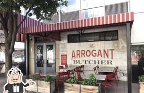 A restaurant named 'The Arrogant Butcher' with outdoor seating and a red and white striped awning.