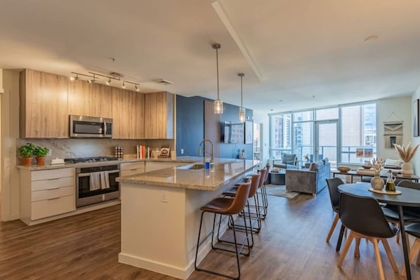A modern kitchen with a central island, bar stools, and a dining area with a view.