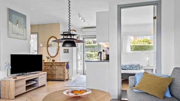 A modern living room with a flat-screen TV, wooden furniture, a round coffee table with fruit, and a view of the outdoors. - 2 bedroom amazing home in Svaneke (Svaneke)