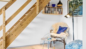 A cozy room with a wooden staircase, a bookshelf, a chair with a fluffy cushion, a small table with cups, and a painting on the wall. - 2 bedroom amazing home in Svaneke (Svaneke)