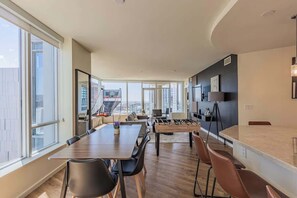 A modern kitchen with a foosball table, a dining area with a large table and chairs, and large windows offering a city view. - DT PHX Stay | Pool, Gym, Balcony, W/D + Parking (Phoenix)