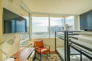A modern hotel room with a large window, a flat-screen TV, a bunk bed, a desk with a lamp, and a chair. - Modern HighRise Sanctuary+Gym+Pool+Prking+W/D (Phoenix)