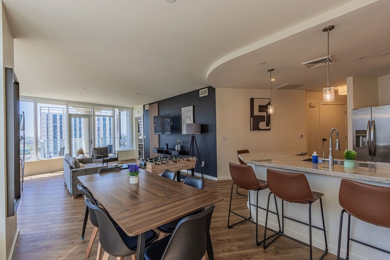 A modern kitchen with a bar area, a dining table with chairs, and a large window providing a view of the city.