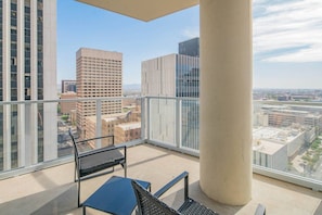 A balcony with a view of city buildings, a table, and two chairs. - Modern HighRise Sanctuary+Gym+Pool+Prking+W/D (Phoenix)