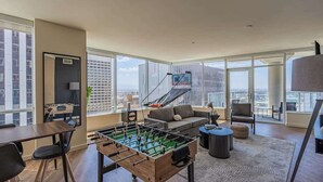 A spacious living room with a foosball table, a sofa, and a staircase leading to an outdoor balcony. - DT PHX Stay | Pool, Gym, Balcony, W/D + Parking (Phoenix)