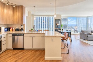 A modern kitchen with a dishwasher, a dining area with a view of the city, and a living room with a sofa.