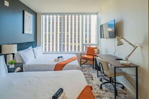 Une chambre d’hôtel avec deux lits, un bureau, une chaise, une télévision et une fenêtre avec des stores.